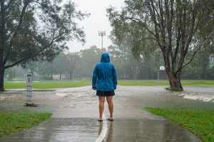 Stormwater and Drainage-Person in a blue rain jacket walking on a flooded pathway during heavy rain in New South Wales